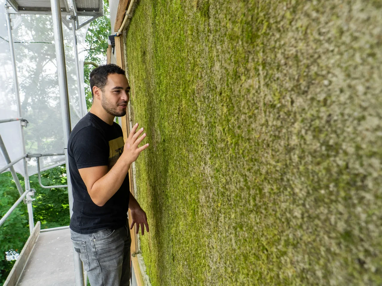 Man leaning against the moss-covered gable facade of the social housing building in Purmerend