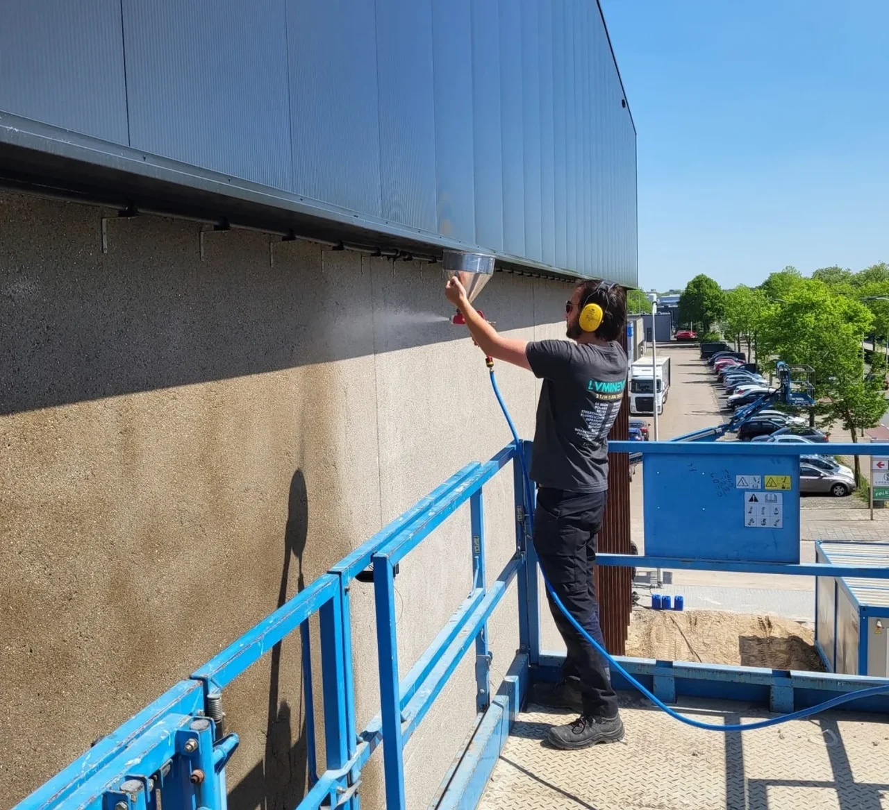 Worker on a lift platform spraying a layer onto the facade of a building